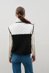 Chaleco con cierre frontal y cuello alto, que combina una parte superior acolchada con diseño de rombos en tonos blanco y marrón, y una parte inferior de corderito negro.