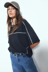 Remera de manga corta con silueta relajada y costuras a la vista en color blanco que contrastan sobre el tejido negro. Presenta un diseño moderno con terminaciones destacadas.