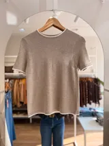 Remera tejida de manga corta con cuello redondo, confeccionada en una mezcla de poliéster, acrílico, poliamida y lana. Presenta un diseño de calce recto en color marrón con detalles de terminaciones en contraste de color blanco en el cuello, las mangas y el ruedo.