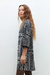 Vestido corto negro con estampado de arabescos en blanco y gris, cuello camisero, mangas largas y corte recto.