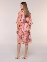 Vestido corto de gasa semitraslúcida con estampado floral en tonos rosados, naranjas y marrones. Posee escote en V, mangas tres cuartos acampanadas con abertura, y un fino lazo ajustable en la cintura. Incluye forro interior a tono.