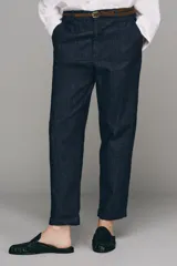 Pantalón chino de tiro bajo color marrón oscuro, con pernera recta y bajo con vuelta. Incluye un cinturón trenzado delgado de color marrón claro. Cuenta con bolsillos delanteros y cierre frontal con cremallera y botón.