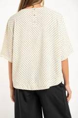 Blusa cruda con estampado de lunares negros, de manga corta y cuello redondo.