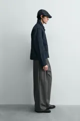 Chaqueta de denim de algodón en color azul oscuro, con cuello solapa y manga larga. Presenta cierre frontal con cremallera oculta bajo una solapa con alamares metálicos, bolsillo de vivo en el pecho y bolsillos de plastrón con solapa en la cadera.