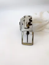 Cinto de cuero con forro de cuero, estampado animal print de vaca en blanco y negro, con hebilla metálica rectangular color bronce y broche suizo.