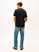 Remera de algodón de corte clásico y cuello redondo, color negro. Presenta un diseño gráfico con el nombre de la marca en tipografía cursiva y un parche rectangular con la inscripción 'Championship Team 1985' en el pecho. Incluye el logo de la bandera de la marca bordado en la manga.