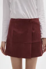 Falda mini de gamuza sintética color bordó, con diseño cruzado y cierre de botón frontal.