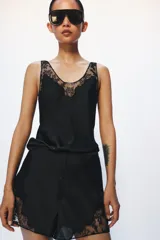 Shorts satinados de tiro medio y cintura elástica, color negro, con detalles de aplicación de encaje a tono en los laterales y cierre frontal de botones.