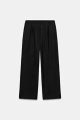 Pantalón negro de tiro medio con pierna ancha y cierre frontal de cremallera con dos botones dorados decorativos.