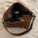 Bolso tipo hobo de eco cuero con textura símil gamuza color marrón rojizo. Presenta detalles de cuero liso color caramelo en la base y tiras ajustables en los laterales.