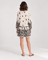Vestido corto color beige con estampado ornamental en color negro, escote en V con cordones y borlas colgantes, y mangas largas.
