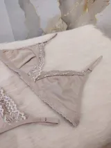 Conjunto de lencería compuesto por un bralette triangular y una bombacha tipo colaless, confeccionados en algodón color nude con delicados detalles de encaje en los bordes.
