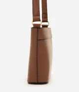 Cartera bandolera pequeña color beige con ribetes marrones, de la marca Satinato. Presenta cierre de cremallera, asa larga ajustable y detalle de placa metálica dorada con el logo en el frente.