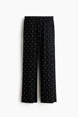 Pantalón de pijama confeccionado en punto pointelle suave, color negro con estampado de pequeños lunares blancos. Cuenta con perneras levemente acampanadas, cintura elástica con ribete de volados y cordón ajustable.