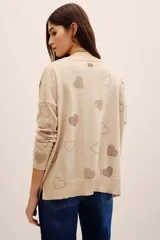 Sweater tejido de punto color beige con diseño holgado, cuello redondo, manga larga y aplicación de corazones formados con tachas brillantes en contraste.