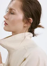 Chaqueta oversize color beige con cuello alto, cierre frontal de cremallera, bolsillos frontales con solapa y mangas largas.
