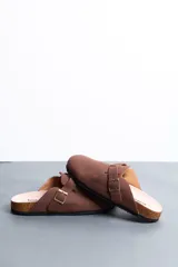 Sandalias estilo zueco de hombre, color marrón, con capellada cerrada, tira con hebilla ajustable lateral y suela de corcho y goma.