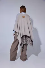 Ruana tejida en lana lambswool con diseño de bloques de color y tramas geométricas. Presenta cierre frontal con doble cursor y tiradores de cuero, permitiendo diferentes formas de uso.