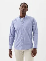 Camisa de manga larga confeccionada en tejido de popelina con diseño de rayas verticales finas en color azul y blanco. Presenta cuello abotonado, cierre frontal con botones y un bolsillo en el pecho.