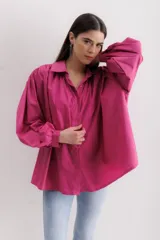 Camisa fucsia de algodón, corte holgado, con cuello camisero, cierre frontal con botones y mangas largas abullonadas con puños abotonados.