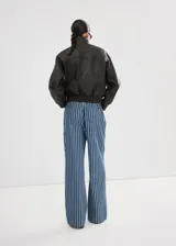 Pantalón estilo tejano vaquero de algodón con diseño largo y recto, tiro medio y estampado de rayas. Cuenta con dos bolsillos laterales y cierre de lazo en la cintura.
