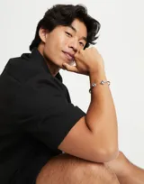 Pulsera rígida de aleación de metales bañada en plata de ley, con dos cristales facetados verdes en forma triangular en los extremos.