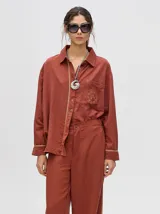 Pantalón de corte holgado y tiro alto con caída recta, color azul petróleo. Presenta una franja lateral decorativa en tonos rojo y amarillo que recorre la pierna, a juego con la camisa de la misma línea.