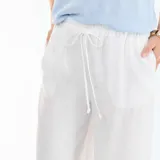 Pantalón de lino blanco de corte ancho, con cintura elástica ajustable mediante cordón y bolsillos laterales.