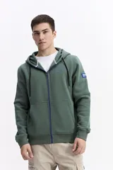 Campera con capucha y cierre frontal, color crema, con bolsillo canguro. Presenta un estampado de texto en el pecho y detalles en el puño.