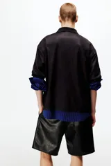 Camiseta de futbol de manga corta con corte holgado, color negro con estampa sutil y bandas blancas con rombos en las mangas. Presenta cuello en V con solapa y esc11udo bordado en el pecho.