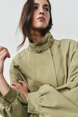 Cazadora de color verde militar, con cuello alto, manga larga abullonada con puños y cierre frontal con botones a presión ocultos. Incluye un cinturón ajustable del mismo tejido para entallar la cintura y bolsillos delanteros de vivo.