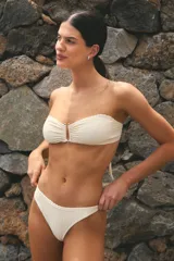 Conjunto de bikini color hueso, confeccionado en lycra texturada. El corpiño es strapless con tiras ajustables y hebilla metálica en el centro. La bombacha es vedetina y está forrada.