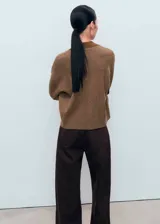 Cardigan de punto fino color marrón, con cuello en pico, cierre frontal de botones y dos bolsillos de parche delanteros. Presenta un diseño recto de manga larga con cuello tipo polo en un tono más oscuro.