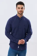 Camisa de lino y algodón color beige, de manga larga, con cuello mao y cierre frontal con botones. Presenta un pequeño bordado al tono en el pecho.