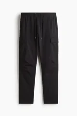 Pantalón cargo negro de corte slim fit, con cintura elástica y cordón ajustable. Presenta bolsillos al bies, bolsillos cargo en las piernas con solapa y botones a presión ocultos, y bolsillos traseros con solapa. Las piernas son ajustadas con costuras y pinzas en las rodillas.