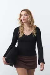 Top de tejido acanalado negro, con escote en V, mangas largas con terminación acampanada y ajuste al cuerpo.