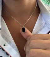 Collar con cadena de eslabones tipo caja plateada y un dije rectangular con borde plateado y centro de piedra negra pulida.