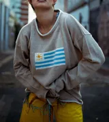 Sweater de hilo de algodón en color beige con diseño tejido de la bandera de Uruguay en el centro. Presenta cuello redondo, mangas largas y un corte holgado.