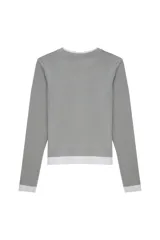 Camiseta de manga larga con diseño de doble capa, confeccionada en jersey suave y elástico. Presenta un calce ajustado, cuello redondo y un estilo minimalista que combina una capa superior en color verde grisáceo con una capa inferior en color blanco.