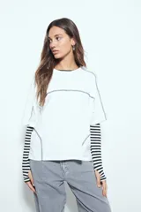 Remera de manga corta con silueta relajada y costuras a la vista en color blanco que contrastan sobre el tejido negro. Presenta un diseño moderno con terminaciones destacadas.