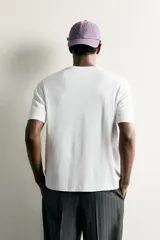 Camiseta regular fit blanca de manga corta y cuello redondo, con un estampado gráfico en el frente que ilustra ropa y accesorios.