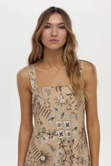 Vestido corto camel de lino y viscosa, con escote cuadrado, breteles anchos y diseño con godets. Presenta un estampado artesanal en tonos marrones y blancos.