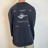 Buzo negro de corte oversize con estampado de concha marina y texto en la espalda.