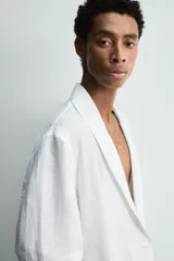 Blazer de corte relajado confeccionada en tejido de lino. Presenta cuello chal, manga larga, bolsillos de plastrón en la parte frontal y cierre cruzado con botones.