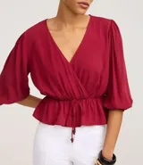 Blusa color vino tinto, con escote cruzado en V, mangas tres cuartos abullonadas con elástico en el puño y peplum ajustado en la cintura con lazo regulable.