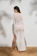 Vestido largo de tejido de punto blanco, con escote profundo en V, detalle de argolla frontal, mangas largas y tajo lateral en la falda.