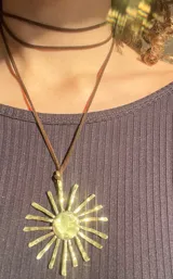Collar con dije dorado en forma de sol con rayos texturizados y cordón negro.