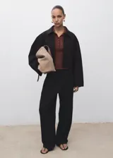 Chaqueta corta de diseño recto con cuello camisero, cierre frontal de botones y dos bolsillos de parche laterales. Presenta manga larga y forro interior.