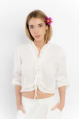 Blusa corta blanca de lino con mangas 3/4 abullonadas, escote en V con volados y cierre con lazos.