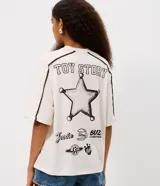 Remera de algodón color crema con cuello redondo y mangas cortas con costuras desplazadas en contraste. Presenta un estampado frontal grande con los personajes de la película Toy Story.